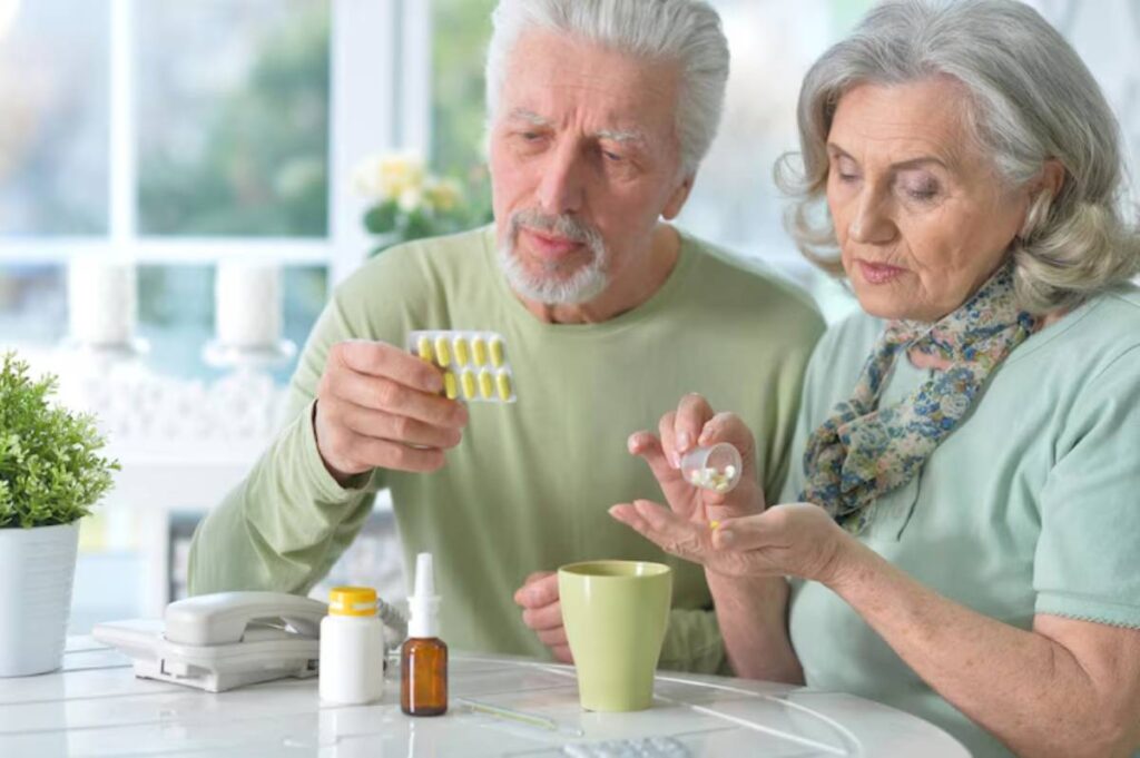 Two elderly individuals are seated at a table, discussing medication while surrounded by small bottles and a cup.
