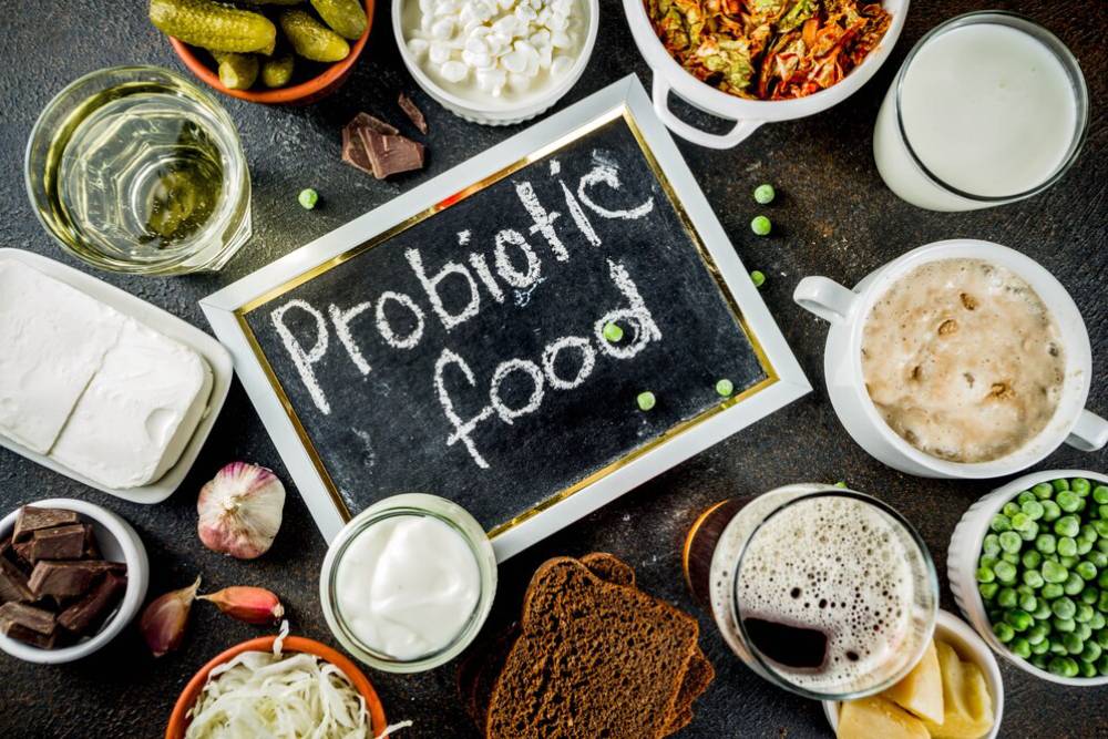 A tabletop spread of probiotic foods, including drinks, pickles, yogurt, chocolate, and a chalkboard labeled - Probiotic food.