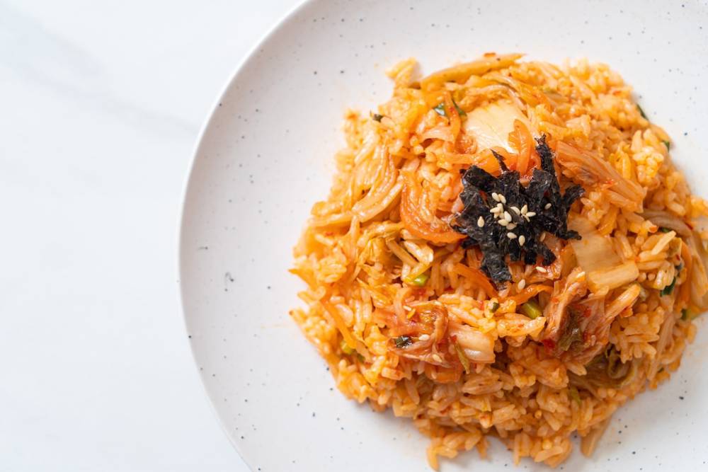 A plate of vibrant kimchi fried rice topped with black seaweed and sesame seeds, showcasing a mix of textures and colors.