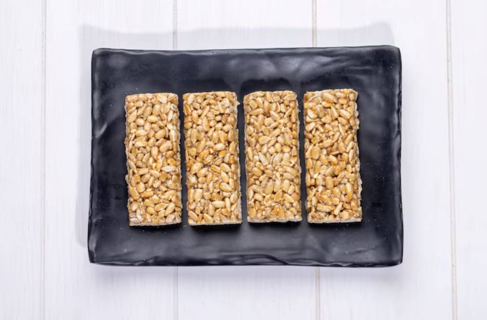 Four rectangular rice snacks bars topped with crispy peanuts on a black plate against a white background.