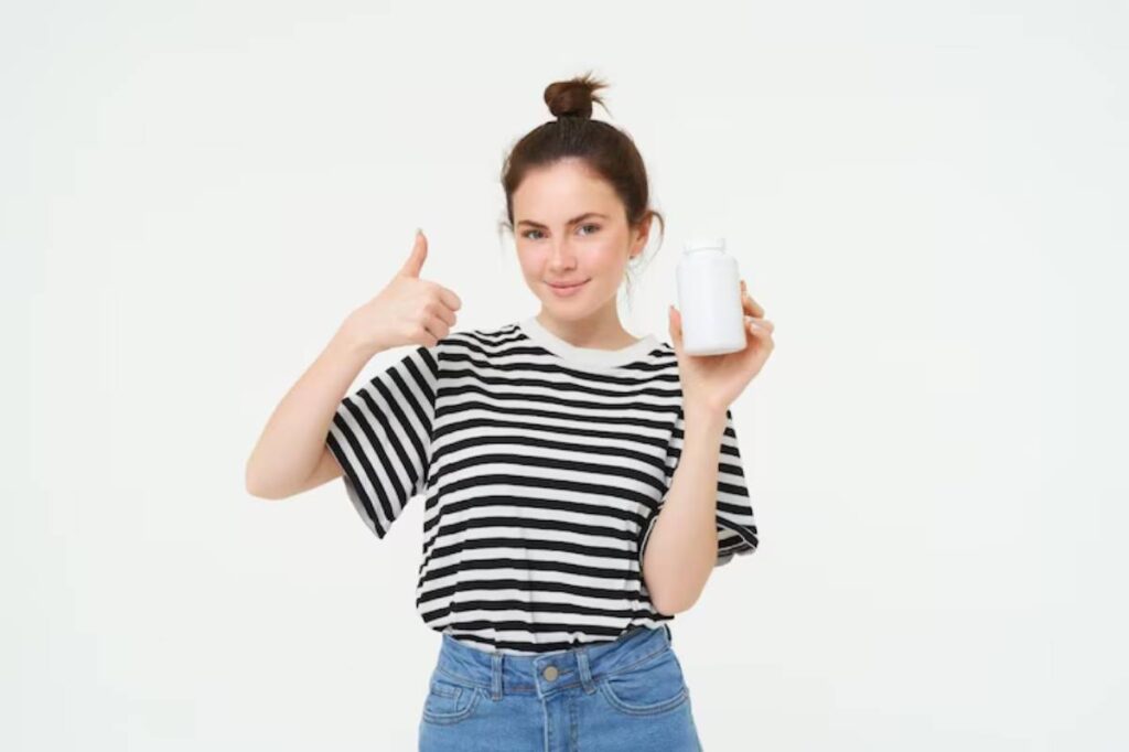 A person wearing a striped t-shirt and denim shorts holds a bottle and gives a thumbs-up, standing against a plain white background.