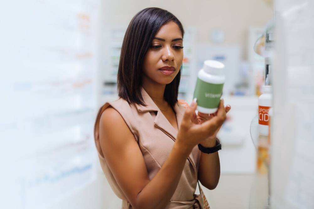 A woman read label of supplement and  products kept on a shelf in a bright pharmacy setting.