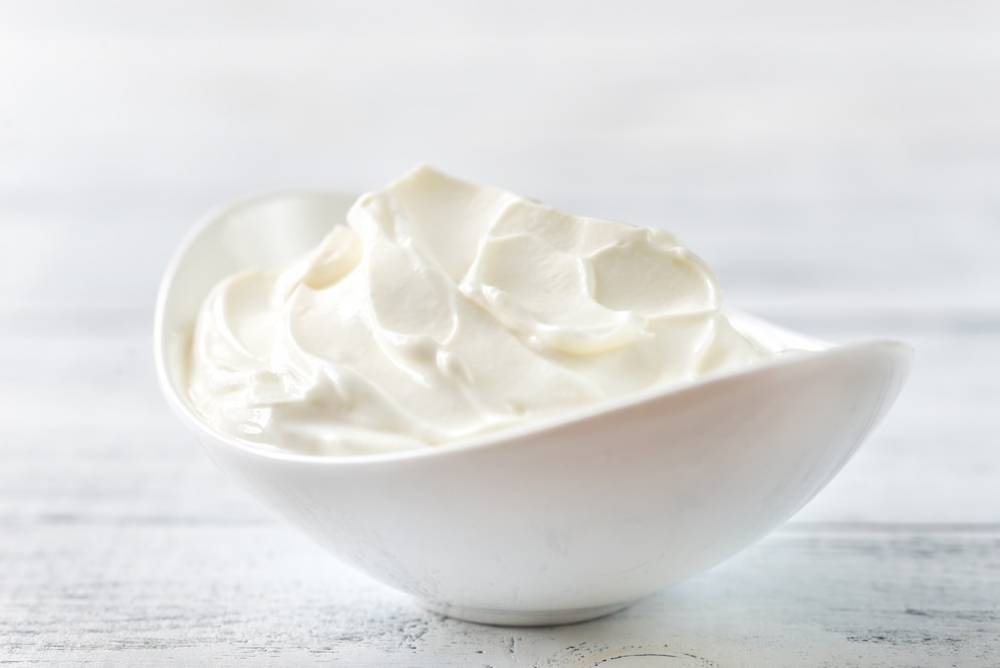 A white bowl filled with  yogurt, resting on a light wooden surface.