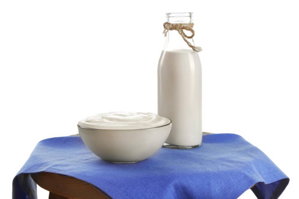 A bowl of  yogurt sits next to a glass bottle of milk, both on a blue cloth-covered table.