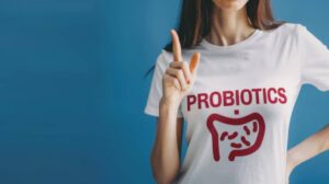 A woman gestures with one finger raised while wearing a white t-shirt that reads 'PROBIOTICS,' featuring a graphic of intestines.