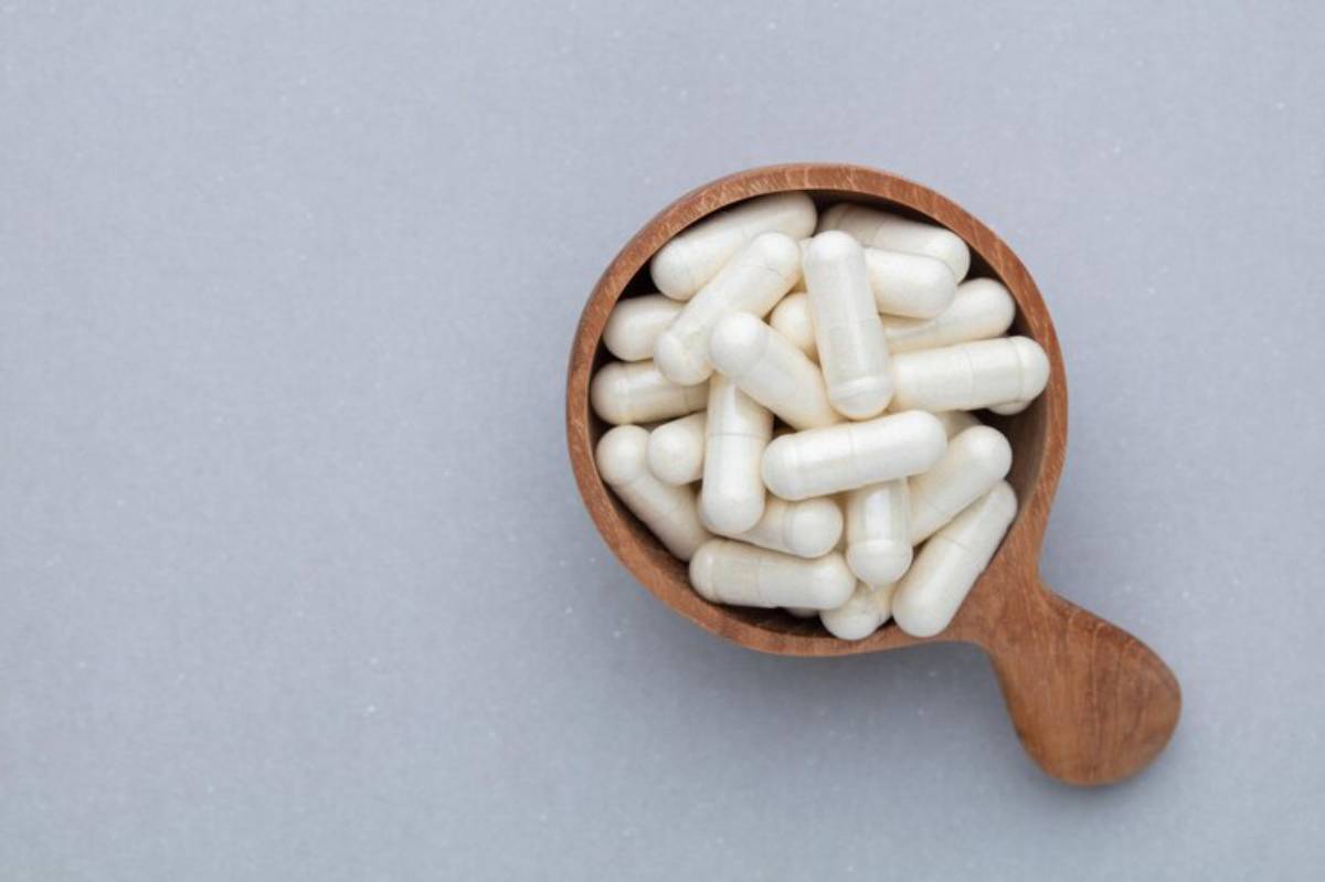 A wooden scoop filled with white capsules rests on a light gray background.